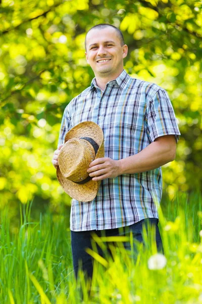 Jonge man in stro hoed buiten in een tuin — Stockfoto