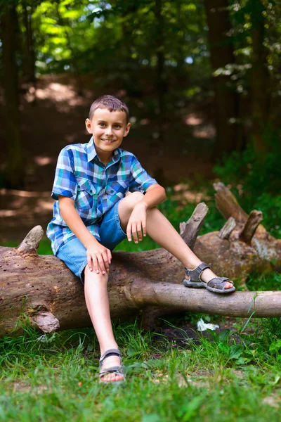 Kind sitzt im Freien auf einem Baumstamm — Stockfoto