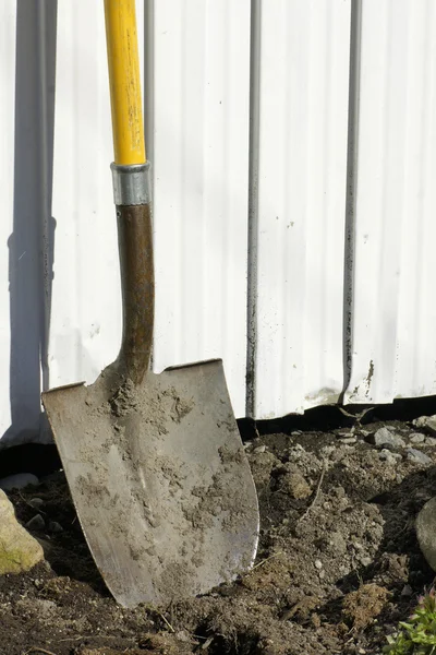 Shovel in earth against garden shed — Stock Photo, Image