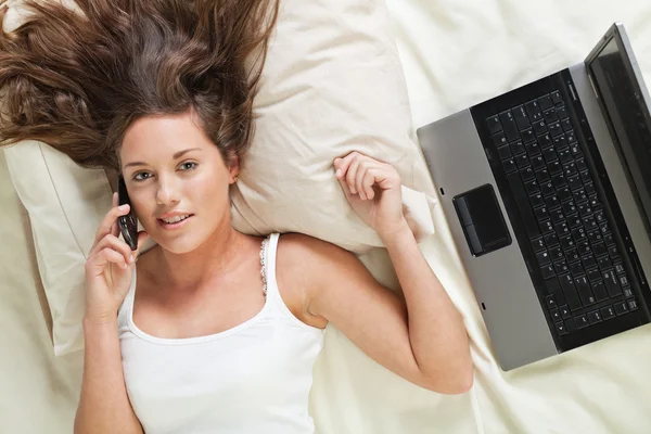 Genç kadın yatakta telefonu ve laptop — Stok fotoğraf