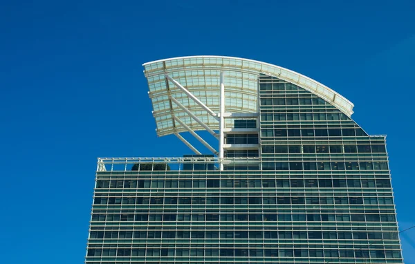 Современная офисная башня из голубого стекла с изогнутой белой крышей под небом — стоковое фото