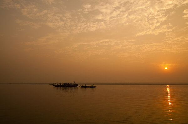 A stunning sunrise looking over the holiest of rivers in India. The Ganges. Silhouettes of boats dapple the horizon.