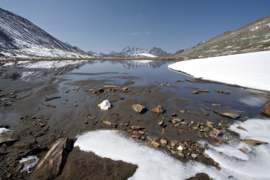 Stones and snow near mountain lake. The pass Baikonur, Sayan mountains. clipart