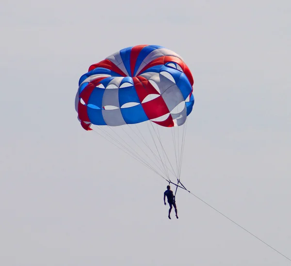 Pára-quedas descendo com um paraquedas contra o céu azul — Fotografia de Stock
