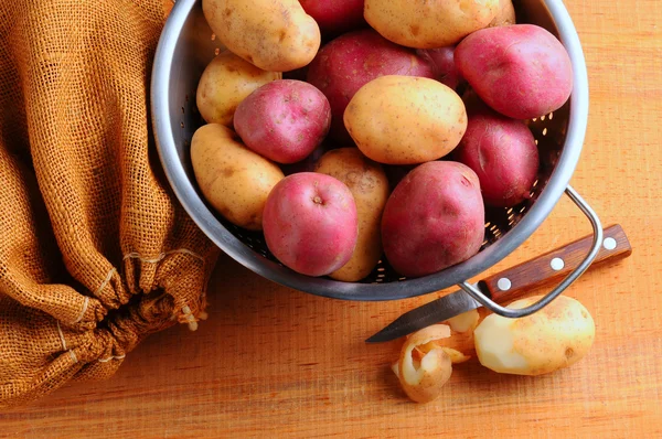 Kartoffeln im Sieb mit Kleckerbeutel und Schälmesser — Stockfoto