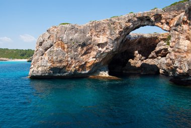 Transparent water and the natural rocky arch at Cala Antena, Maj clipart