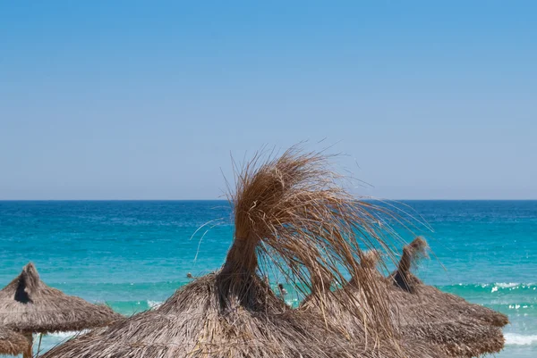 Strawy şemsiye altında Akdeniz önünde mavi s işareti kaldırın. — Stok fotoğraf
