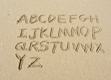 Alphabet letters handwritten in sand on beach clipart