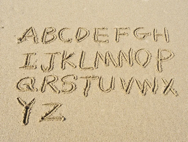 Lettere in alfabeto scritte a mano in sabbia sulla spiaggia — Foto Stock