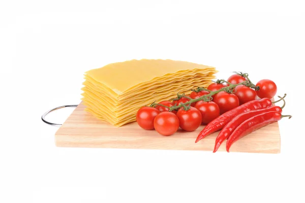 Massas de lasanha e tomate e pimentas vermelhas sobre tábua de corte isolada sobre branco — Fotografia de Stock