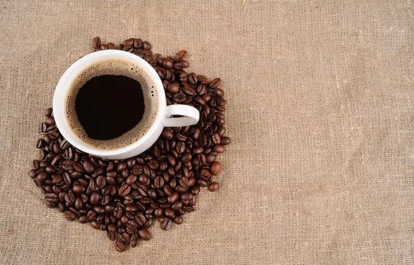 Grains de café avec tasse sur un sac rugueux — Photo