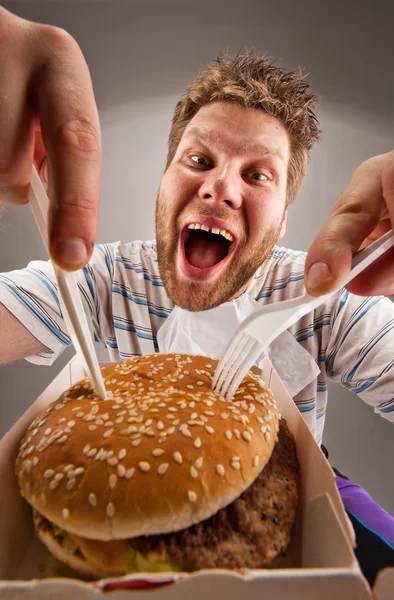 Muž s nožem a vidličkou jíst hamburger — Stock fotografie