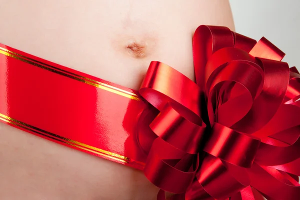 Hamile kadının karın üzerinde kırmızı yay — Stok fotoğraf
