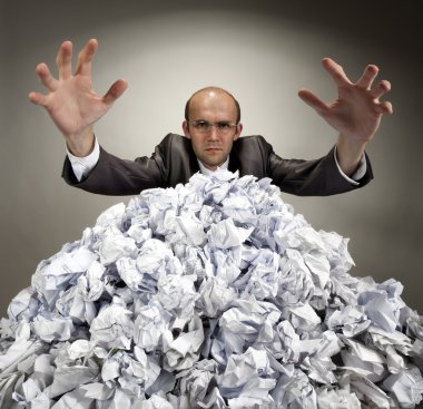 Serious businessman reaches out from crumpled papers clipart