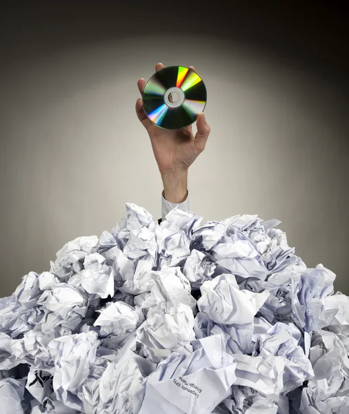 Hand with CD reaches out from heap of papers — Stock Photo, Image
