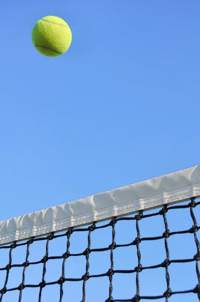 Bola amarilla de tenis volando sobre la red — Foto de Stock