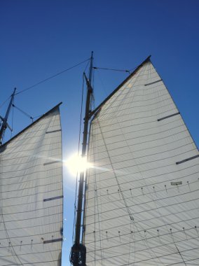 Sun Between Mainsail and Foresail of Schooner Sailboat clipart