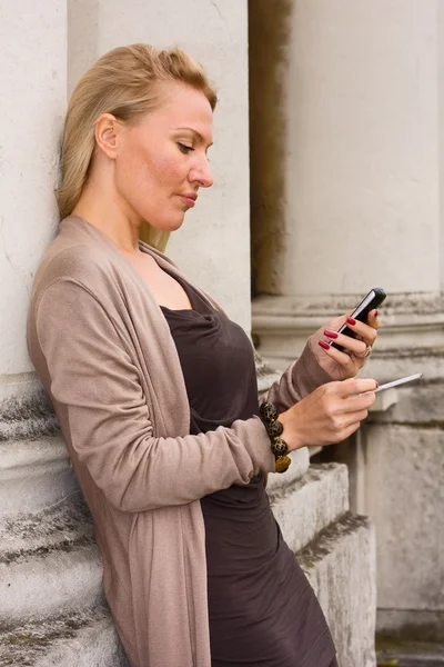 Mujer fumando y sosteniendo un teléfono . — Foto de Stock