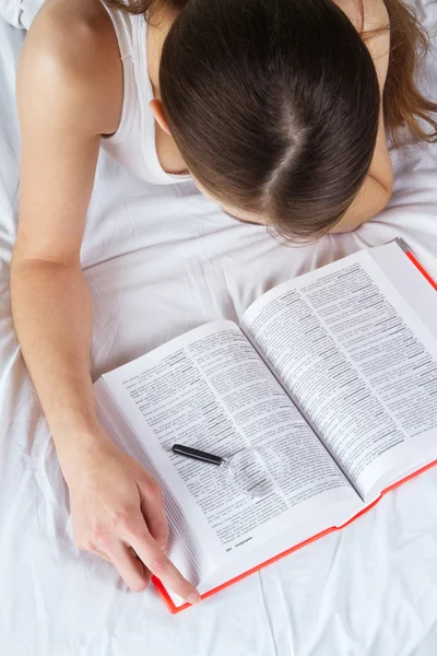 Ung kvinna läser en bok i sängen — Stockfoto