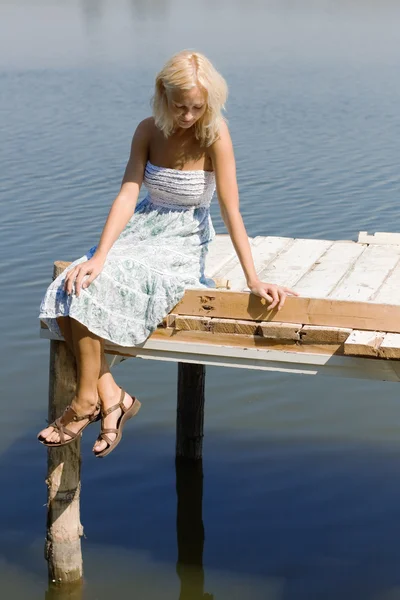 Chica sentada en un muelle en la orilla del río — Foto de Stock