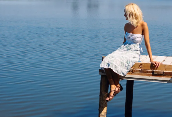 Девушка, сидящая на пирсе на берегу реки — стоковое фото