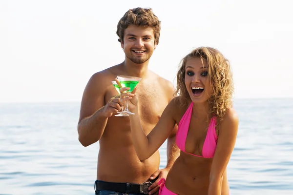 Молодая пара на берегу моря с коктейлями — стоковое фото