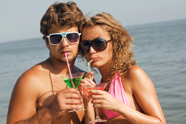 Молодая пара на берегу моря с коктейлями — стоковое фото