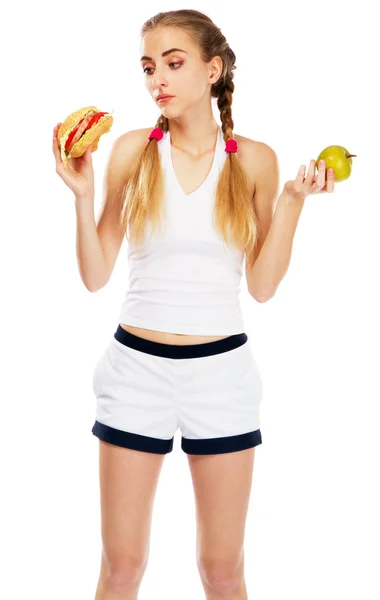 Mujer joven sosteniendo una hamburguesa y una manzana — Foto de Stock