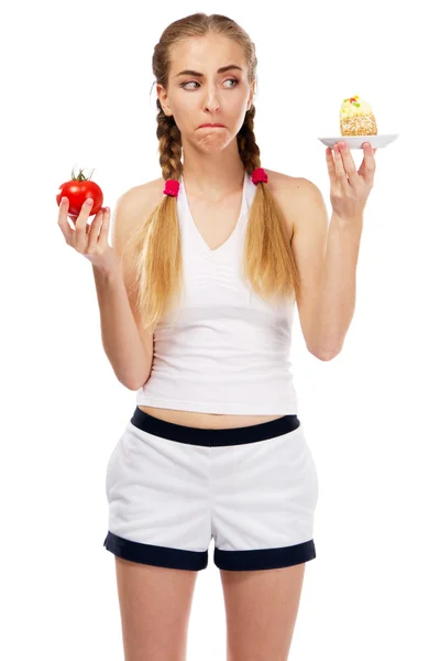 Young woman deciding on a tomato and a cake — Stock Photo, Image