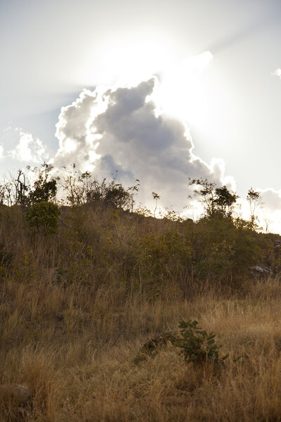 Zambian hill covered in dry grass wit the sun behind clouds in the background