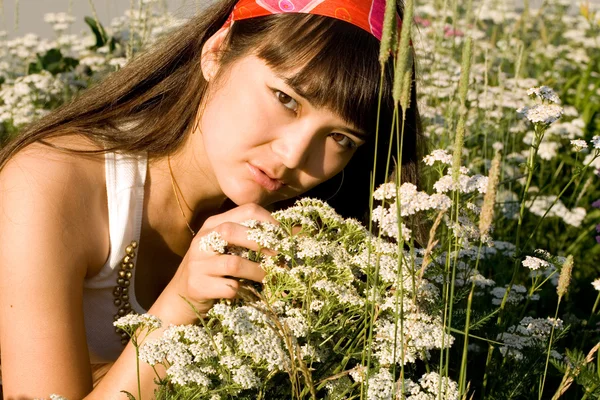 Schönes Mädchen sitzt auf einer Wiese mit Blumen — Stockfoto