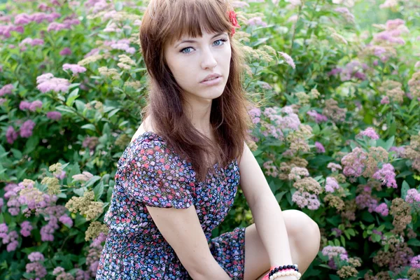 Mooi meisje, zittend op de weide met bloemen — Stockfoto