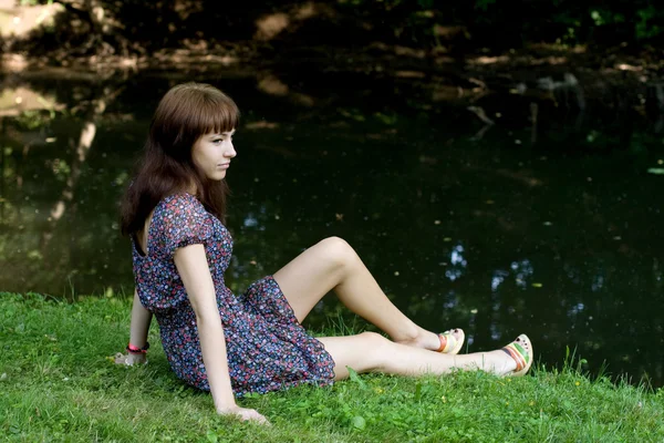 Piękna dziewczyna siedzi na brzegu rzeki — Zdjęcie stockowe