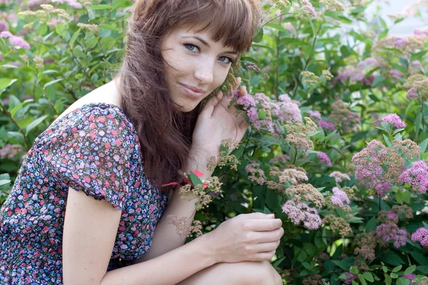 Hermosa chica sentada en el prado con flores —  Fotos de Stock