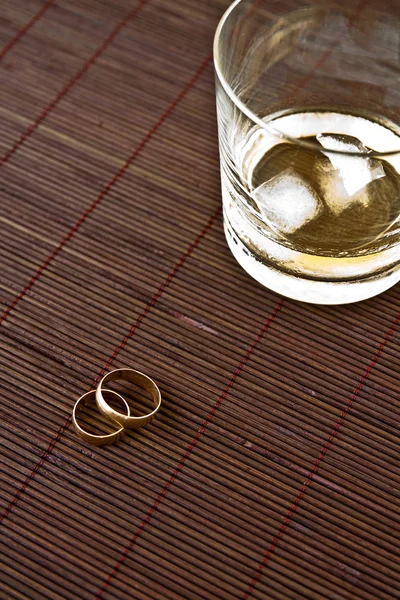 Sklenka alkoholu a snubní prsteny — Stock fotografie