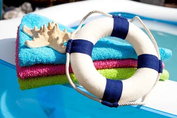 Toalla colorida, boya salvavidas y estrellas de mar en la piscina —  Fotos de Stock
