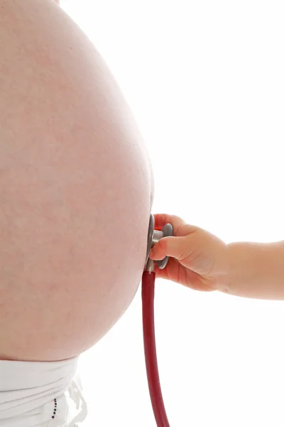 Kinderhand mit Stethoskop auf Schwangerschaftsbauch — Stockfoto