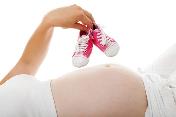 Woman is holding little pink shoes over pregnant belly — Stock Photo, Image