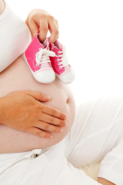 女性は妊娠中の腹の上の小さなピンクの靴を保持しています。 — ストック写真