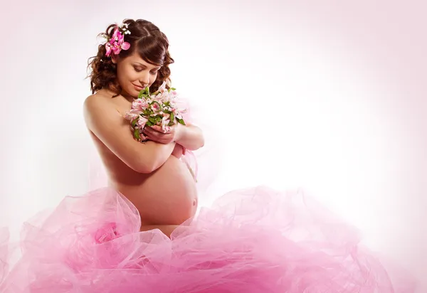 怀孕的女人微笑，低头看鲜花，举行花 — 图库照片