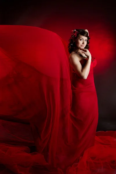 Schöne Frau im roten wehenden fliegenden Kleid. Blick in die Kamera. — Stockfoto