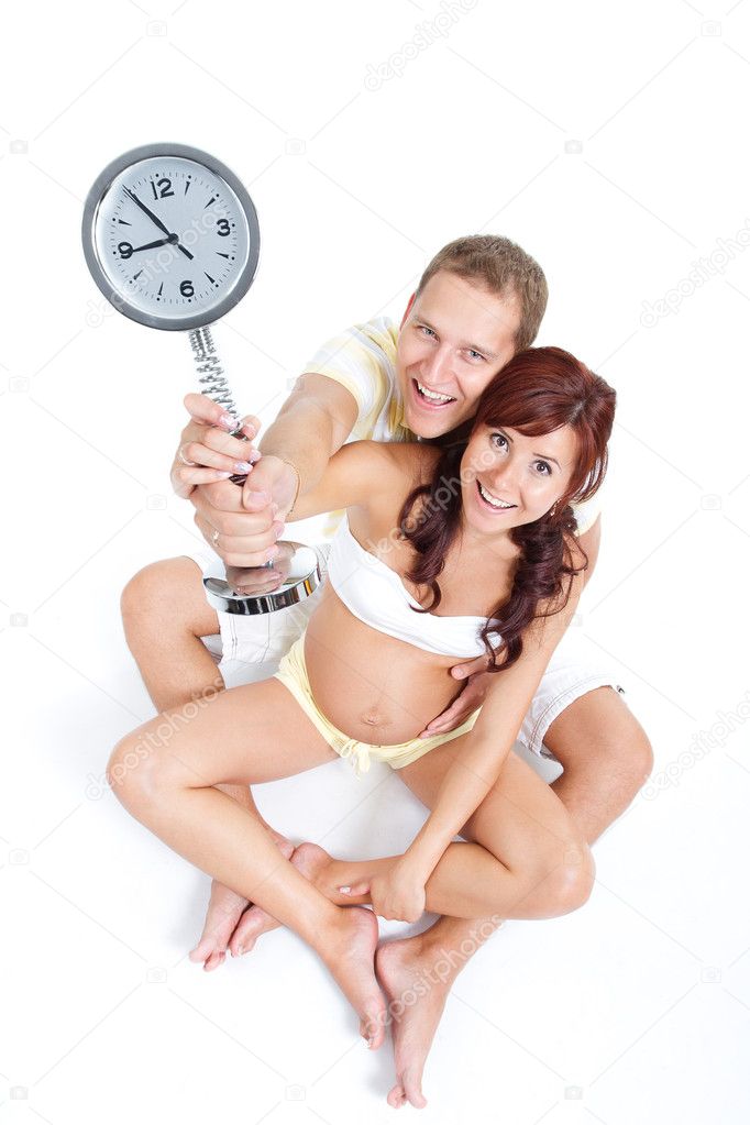 Pregnant woman with husband, holding a clock showing 9th month,