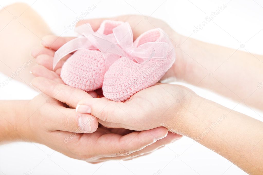 Mother's and father's hands holding pink newborn baby booties. O