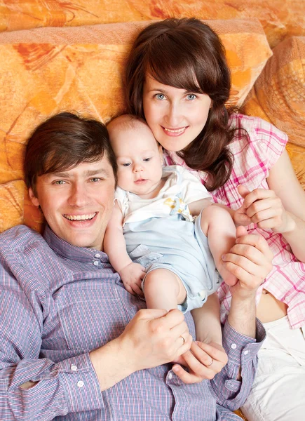 Dreiköpfige Familie legt sich ins Bett, kuschelt und lächelt. — Stockfoto