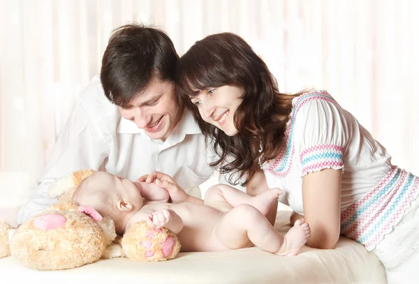Jonge lachende ouders kijken naar baby, spelen met kind. binnen. — Stockfoto