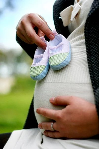 Femme enceinte tenant des chaussures de bébé — Photo