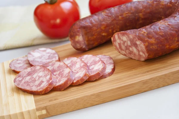 Saucisse fumée sur une planche à découper et tomates fraîches — Photo