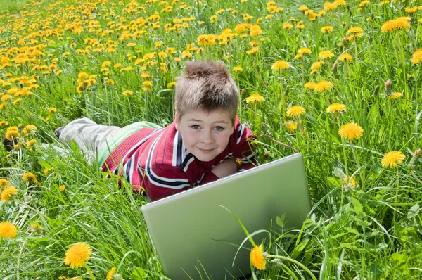 Chlapec s přenosným počítačem, ležící na trávě — Stock fotografie