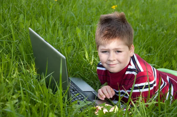 Chłopiec z komputera przenośnego, leżąc na trawie — Zdjęcie stockowe