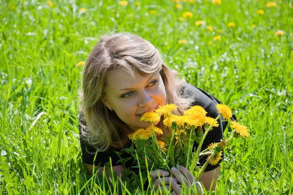 Retrato de uma jovem no gramado com um buquê de dentes-de-leão — Fotografia de Stock